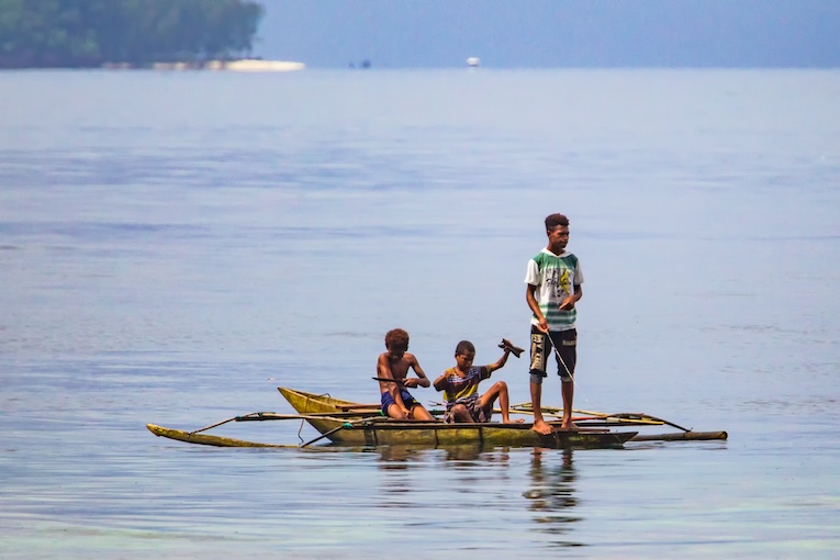 Local boys in traditional fishing canoe, Raja Ampat